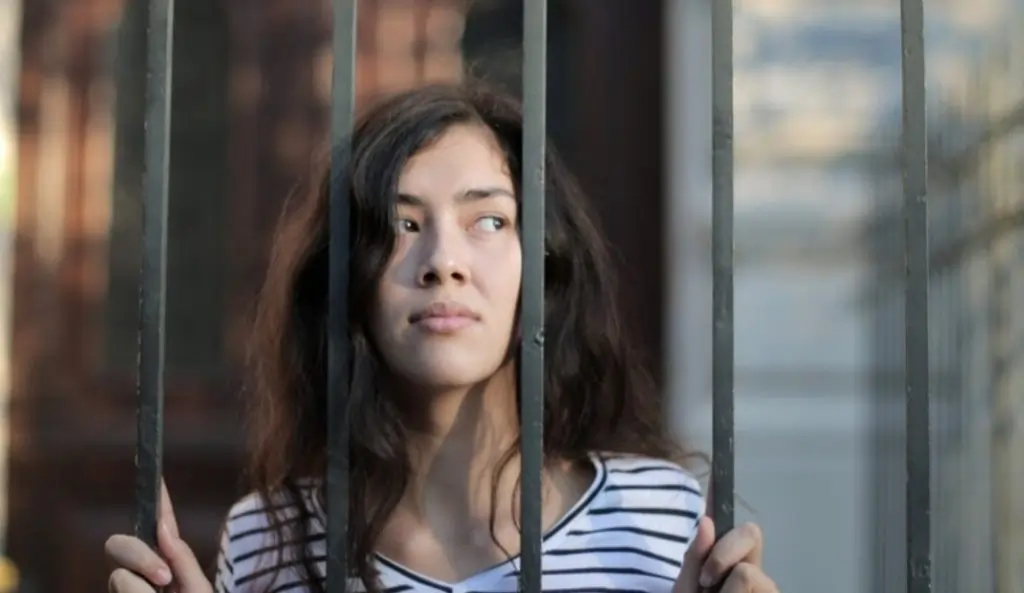 A participant in an escape room, looking through metal bars, demonstrating teamwork, communication, and problem-solving skills.