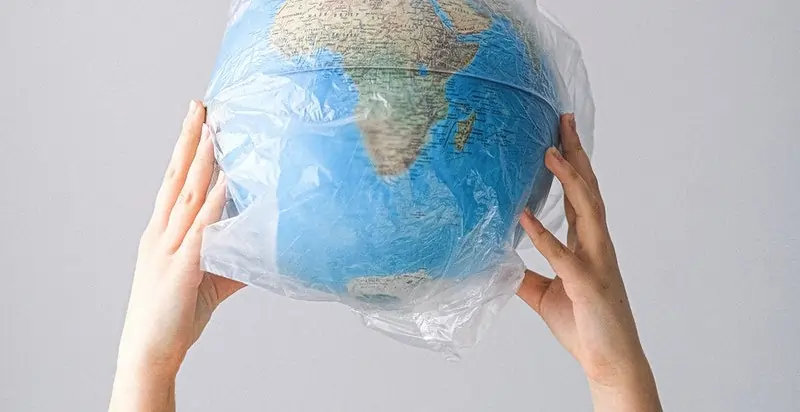 A globe wrapped in a plastic bag, symbolizing the impact of plastic pollution, as part of a STEM activity where kids create a rope from plastic materials to solve a survival challenge on a desert island.