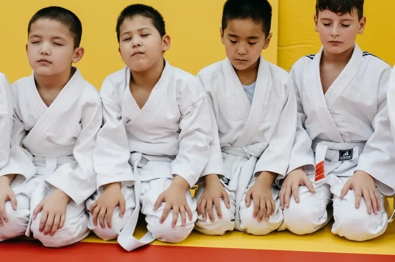 Children dressed in karate clothes meditating, engaging in a STEM activity that promotes focus, discipline, and mental clarity, key skills that support problem-solving and critical thinking in hands-on learning environments.